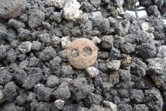 Small button with two holes in it sitting on a bed of rubble