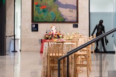 Tiered wedding cake with florals set up under large cactus mural in musuem lobby with cocktail tables nearby
