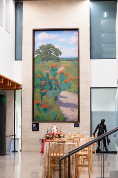 Tiered wedding cake with florals set up under large cactus mural in musuem lobby with cocktail tables nearby