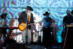 Ray Benson playing his guitar on stage with band members from Asleep at the Wheel