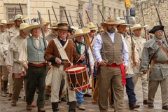 Men in 1830s period attire marching by Long Barrack led by a drummer