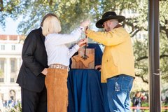 Three people holding a cattle brand and branding a piece of hide