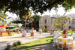 Festive dinner and cocktail tables set up in Alamo Gardens for an event with colorful ribbons and hats bordering the area
