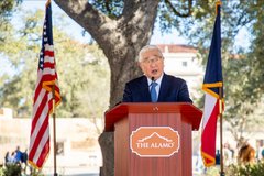 Bexar County Judge Peter Sakai standing a podium flanked by US and Texas flags