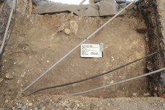 Inside an excavation unit with three pipes going across top surface over the dirt