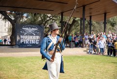 Living historian holding a musket as he walks in front of a crowd
