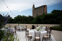 Tables set up for an event with white floral centerpieces and white lines, Emily Morgan hotel in the background