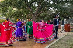 Ballet Folklorico dancers in bright red, purple, green, and pink dresses on a dance floor under a tree
