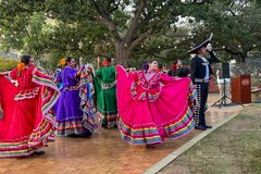 Ballet Folklorico dancers in bright red, purple, green, and pink dresses on a dance floor under a tree