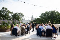 Guests seated at round tables on an outdoor rooftop terrace with string lights