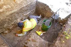 Archaeologist with bright yellow vest digging in an excavation unit