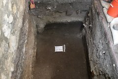 Whiteboard and ruler inside dark dirt floor of an excavation unit