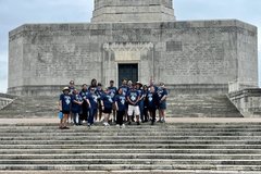 Group of people in navy blue T-shirts standing at the top of stairs outside a presidio