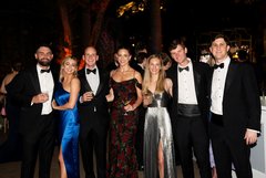 Four men and three ladies dressed in black tie attire smiling at an evening outdoor event