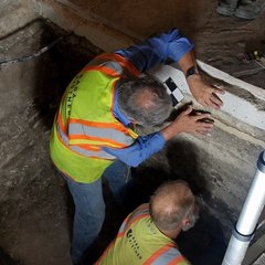 Archaeologists examining stone inside excavation unit