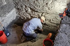 Archaeologist bent over looking inside an excavation unit