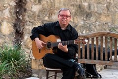 Man sitting in chair playing a guitar in Alamo Hall Patio