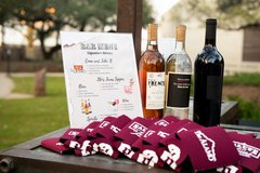 Beverage menu in a plastic frame set next to three bottles of wine and red koozies