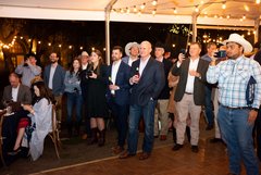 Guests standing in a tented structure listening to remarks at an event