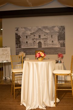 Table with white linen and bright flowers in front of large artwork of Alamo Church in black and white