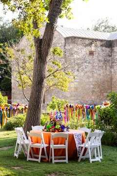Round table with orange linen and white chairs in a grassy outdoor area set up for an event
