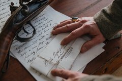 Contact Us Fall Back Image Hands on a handwritten letter and envelope next to a gun