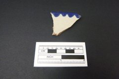 Triangular shaped white ceramic fragment with blue wavy trim