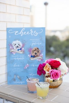 Pink and yellow drinks next to small vase with bright flowers and a cocktail menu on a blue board
