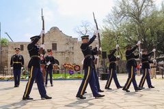 Army soldiers marching in front of the Alamo with rifles facing the sky