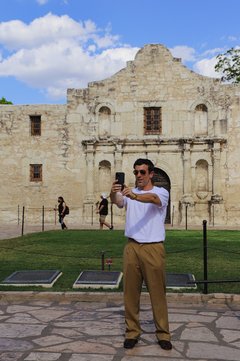 A man taking a picture of himself with his phone outside of Alamo Church