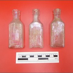 Three glass bottles recovered during excavation next to a ruler to show size