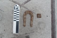 Mule shoe and hardware on a wire background next to a ruler for size