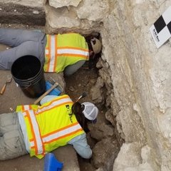 Archaeologists removing dirt in between stones in excavation unit