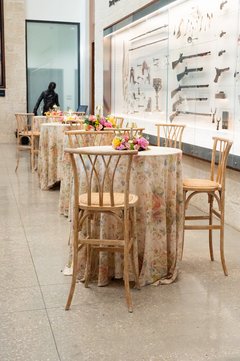 Cocktail tables with floral linens and a small floral centerpiece in a museum gallery area