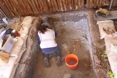 Archaeologist on bended knee facing inside of excavation unit
