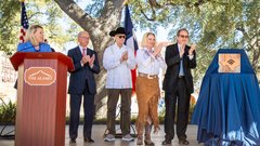 Woman behind a podium and four other people standing on a stage applauding