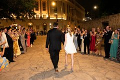 Bride and groom walking towards exit cars between two aisles of guests cheering them on