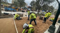 Construction workers in yellow vests digging in a dirt area