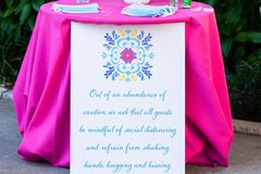 Table with hot pink linens, flowers, and sign with COVID precautions