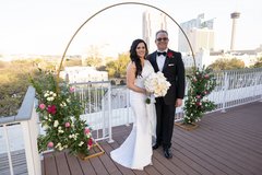 Bride and groom under floral arch on rooftop terrace with view of Alamo Plaza behind them