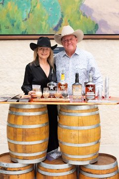 Woman and man in cowboy hats at a bourbon station set up over barrels