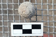Small musket ball on a fenced background next to a ruler for size