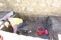 Archaeologist bent over digging inside an excavation unit