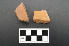 Two light orange ceramic sherd fragments next to a ruler for size