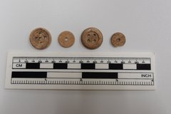 Four brown buttons next to a ruler for size