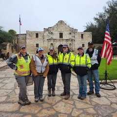Six people in front of Alamo Church, next to a US flag