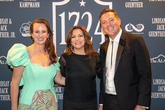 Woman in green gown next to a woman in all black and a man wearing a black tuxedo jacket and a bolo