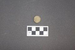 Back side of a round loop shank coin on a gray surface next to a ruler for size