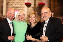 Two women, one in a green dress and one dressed in black, with two men in black tuxedos
