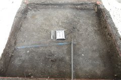 Two utility pipes cross in an excavation unit with a white board and marker in the center